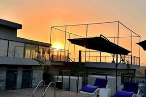 A modern building with a glass facade, a pool area with lounge chairs, and a staircase leading to an upper level. - The Skyluxe (Islamabad)