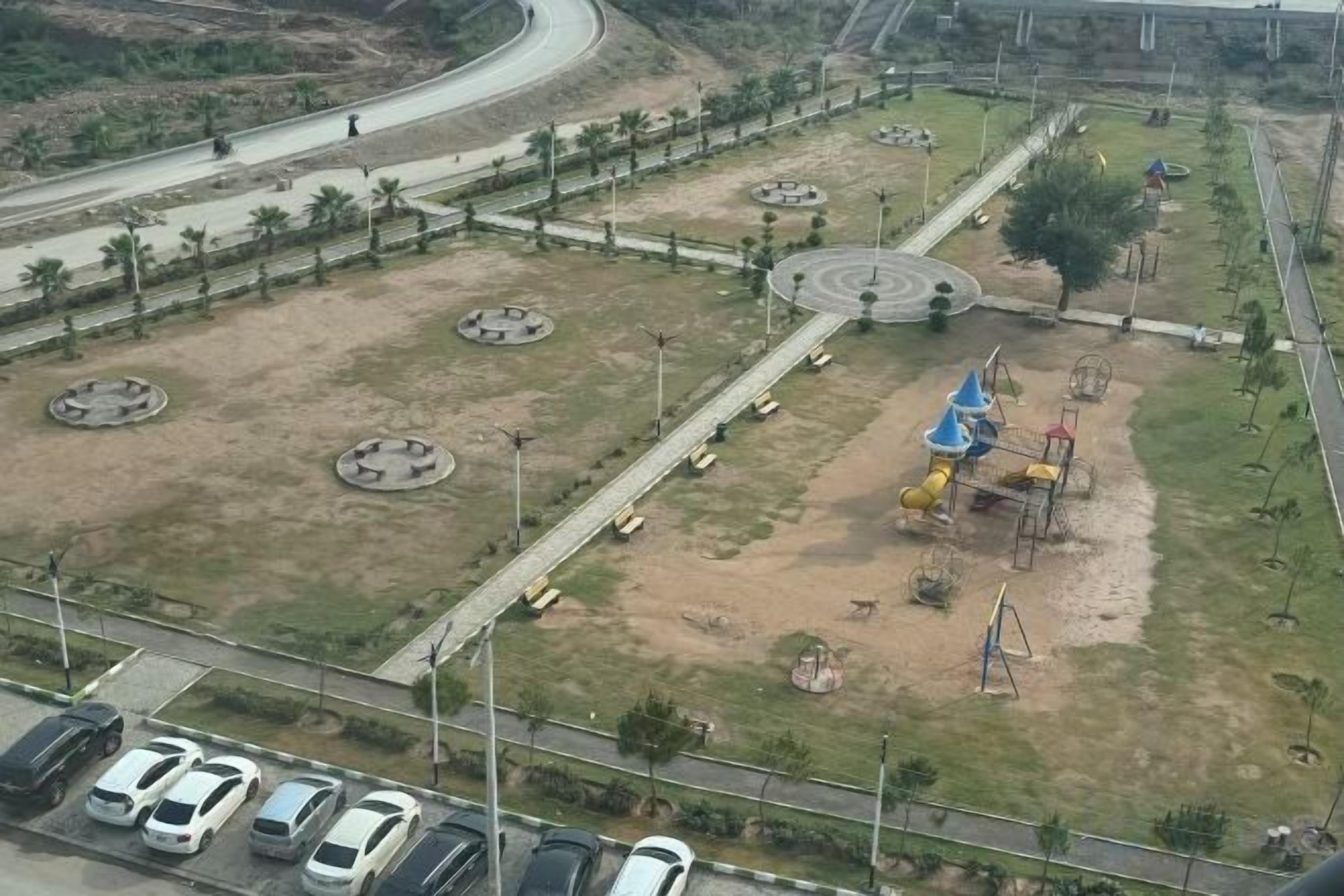 Luftaufnahme eines Parks mit Rundspielflächen, einem Spielplatz und einer Straße mit Autos.
