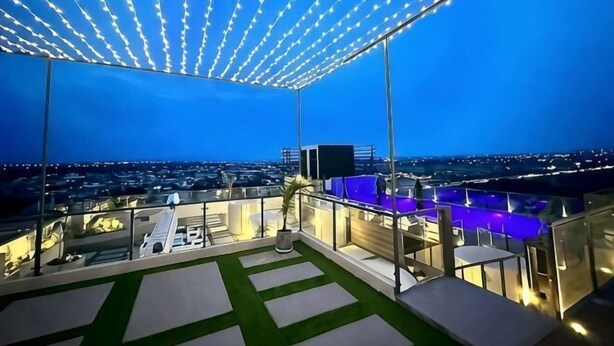 A rooftop terrace with a view of the cityscape, a seating area, and a covered section with string lights. - The Skyluxe (Islamabad)