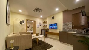 A modern living room with a sofa, coffee table, and TV. There is a kitchen area with a sink and cabinets. - The Skyluxe (Islamabad)