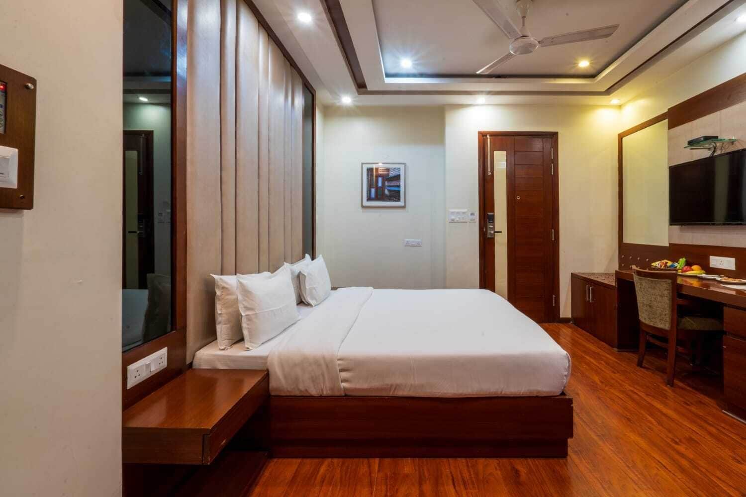 Une chambre d’hôtel avec un lit, un plancher en bois, un bureau avec une chaise, une télévision et une porte.