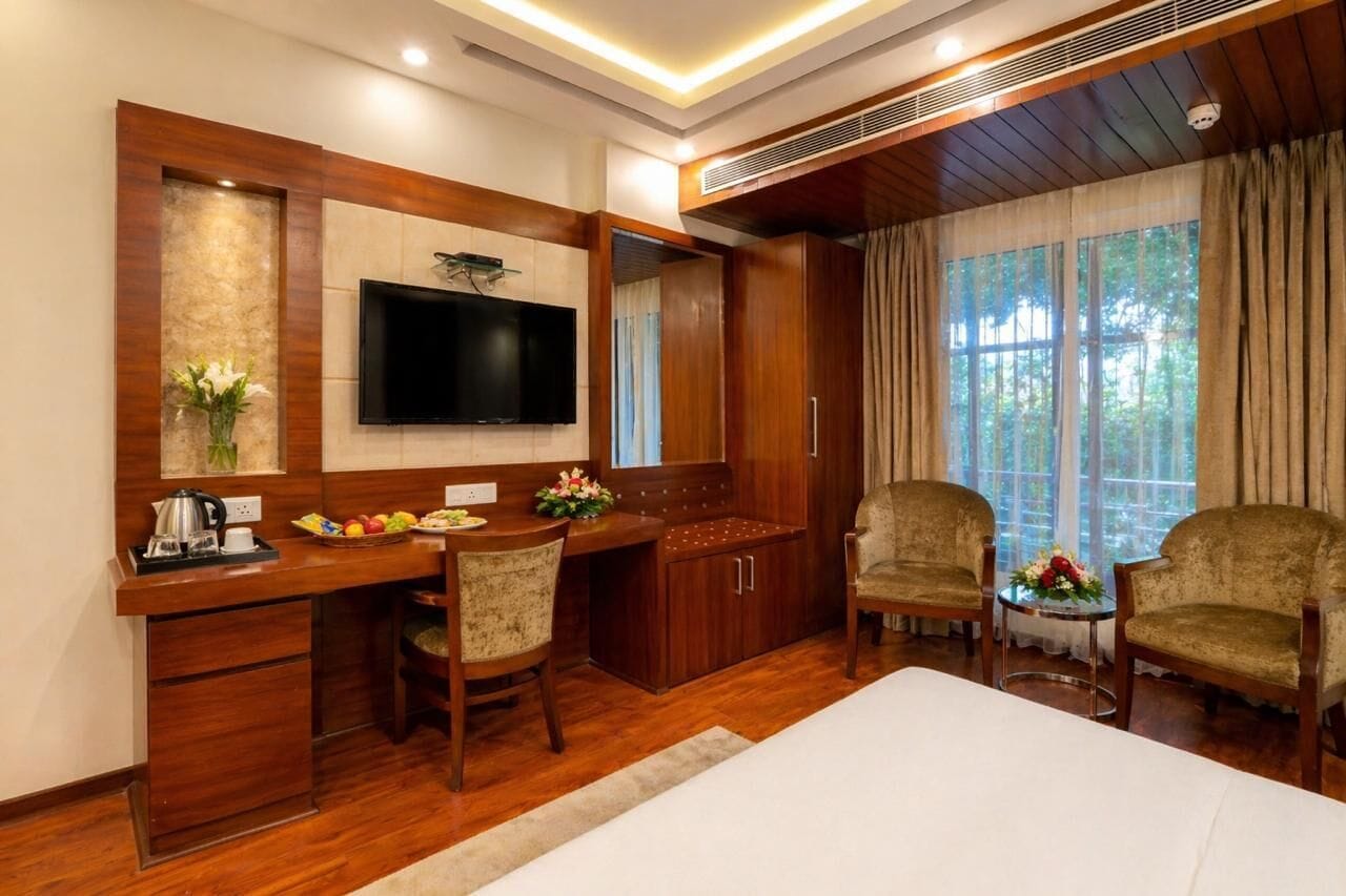 A hotel room with a wooden desk, a flat-screen TV, a bed, and a seating area with two chairs.