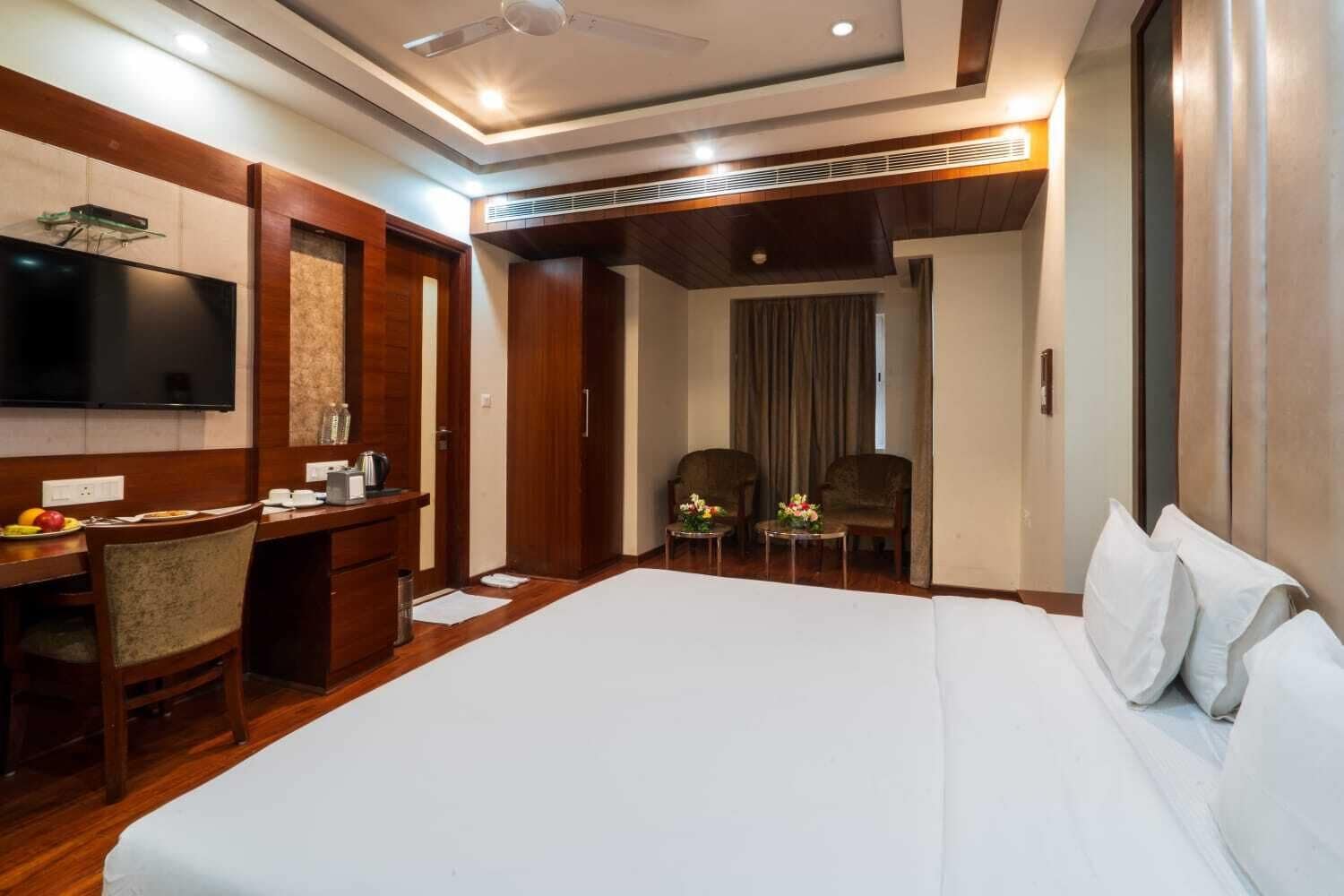 Une chambre d’hôtel avec un grand lit, un bureau avec une chaise, une télévision et une petite table agrémentée de fleurs.