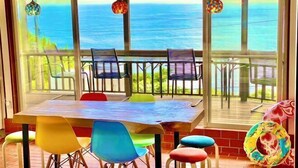 Zona pranzo con vista sull'oceano, con un tavolo in legno e sedie colorate.