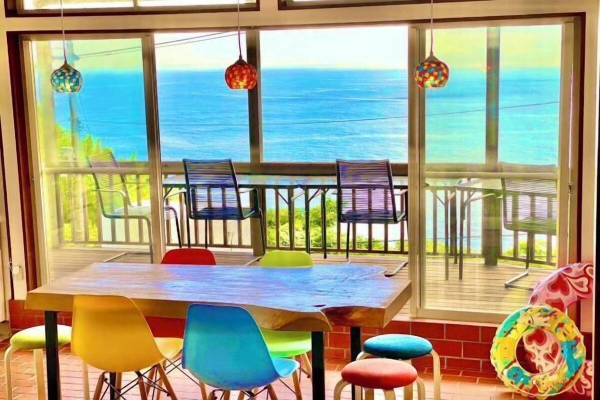 A dining area with a view of the ocean, featuring a wooden table and colorful chairs.