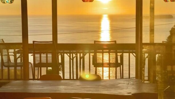Vista da un balcone sul mare al tramonto, con lanterne appese e un tavolo con sedie.