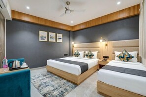 A hotel room with two beds, a desk, a chair, and a ceiling fan. - Hotel Emerald Suites At Delhi Airport (New Delhi)