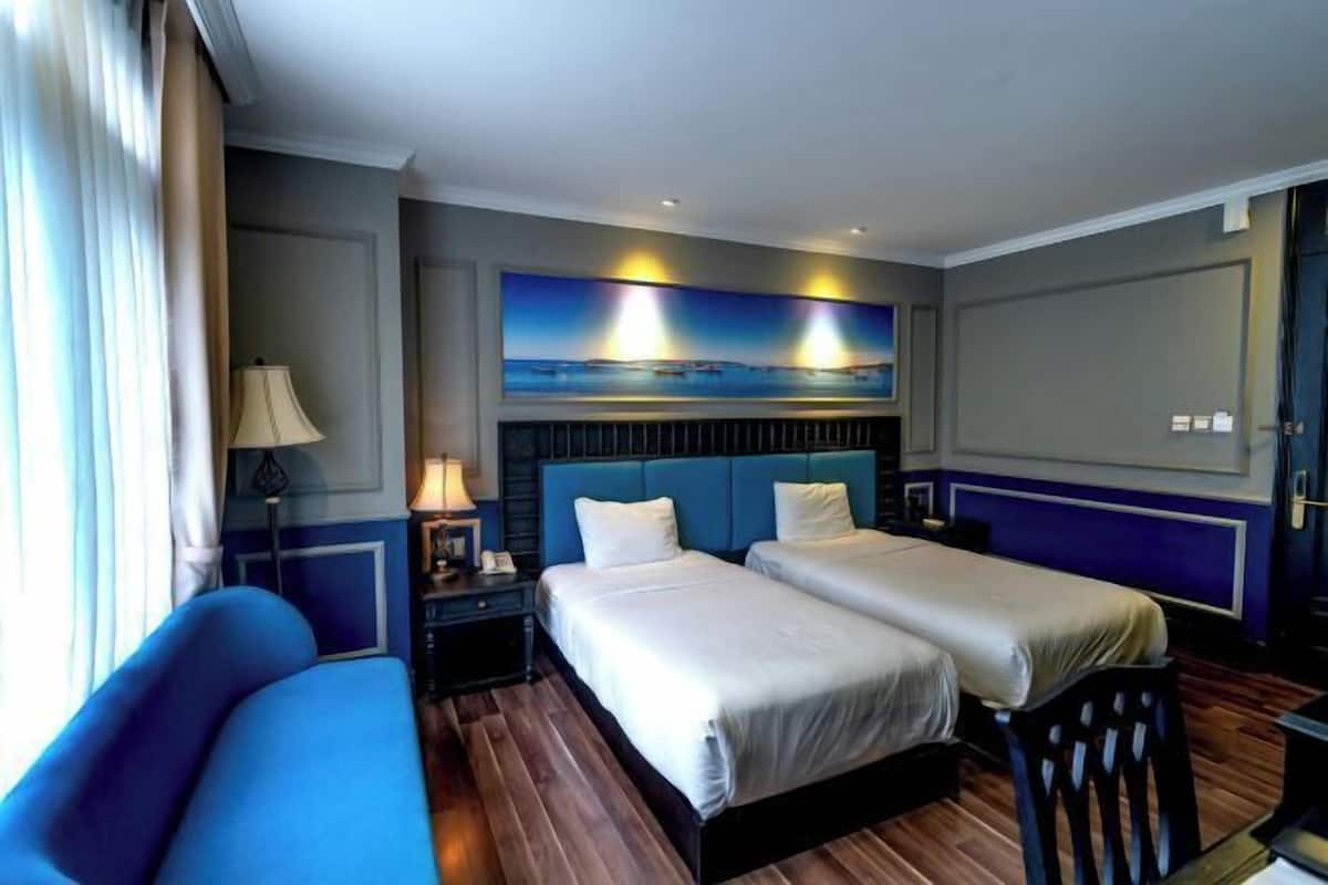 Een hotelkamer met twee bedden, een bank, een nachtkastje, een lamp en een schilderij aan de muur.