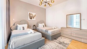 A modern hotel room with two beds, a large mirror, and a chandelier.