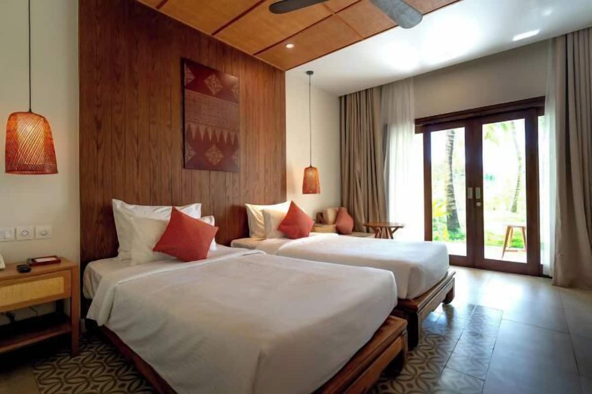 Een hotelkamer met twee bedden, een houten plafond, een groot raam met gordijnen en een vloer met een patroon.
