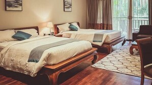 A hotel room with two beds, a wooden headboard, a nightstand, a lamp, a chair, and a view of the outdoors through large windows.
