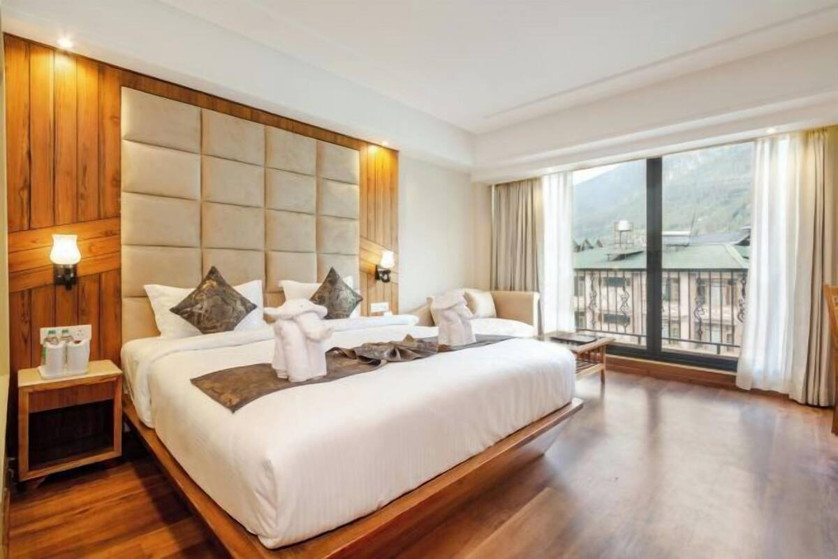 Habitación de hotel con una cama grande, cabecero de madera, lámparas de noche, una mesita de noche, ventana con vistas y un balcón.