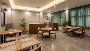 A hotel dining area with multiple tables, chairs, a reception desk, and potted plants.