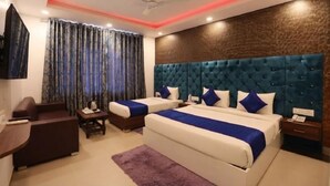 A hotel room with a large bed, two smaller beds, a desk, a chair, a TV, and a ceiling fan.