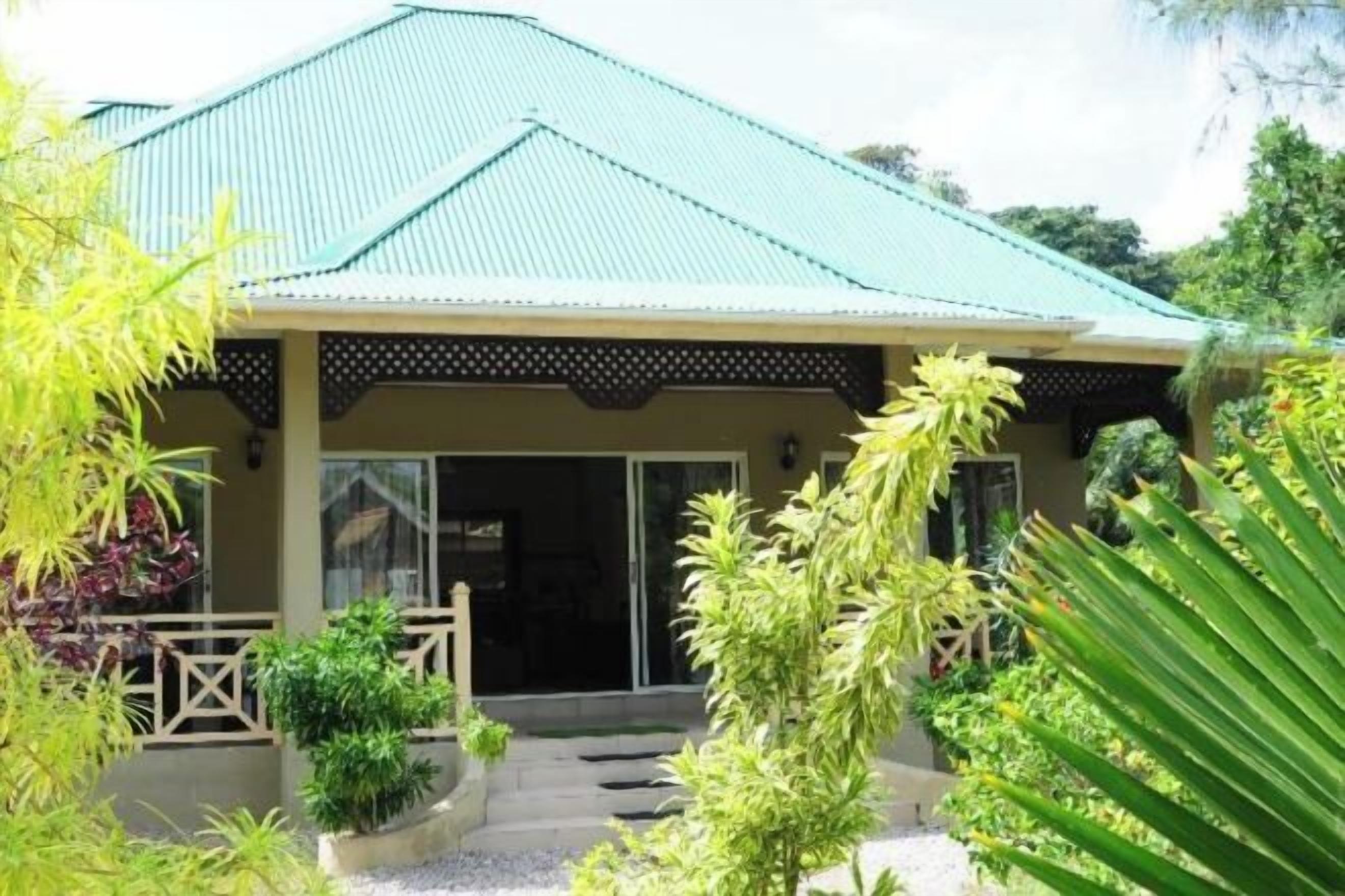 A building with a green roof, a covered entrance, and a garden with various plants.