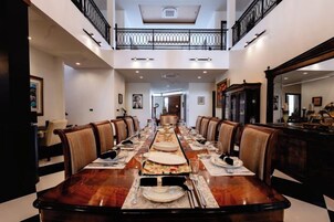 A spacious dining area with a long table set for a meal, flanked by chairs, and a balcony above.