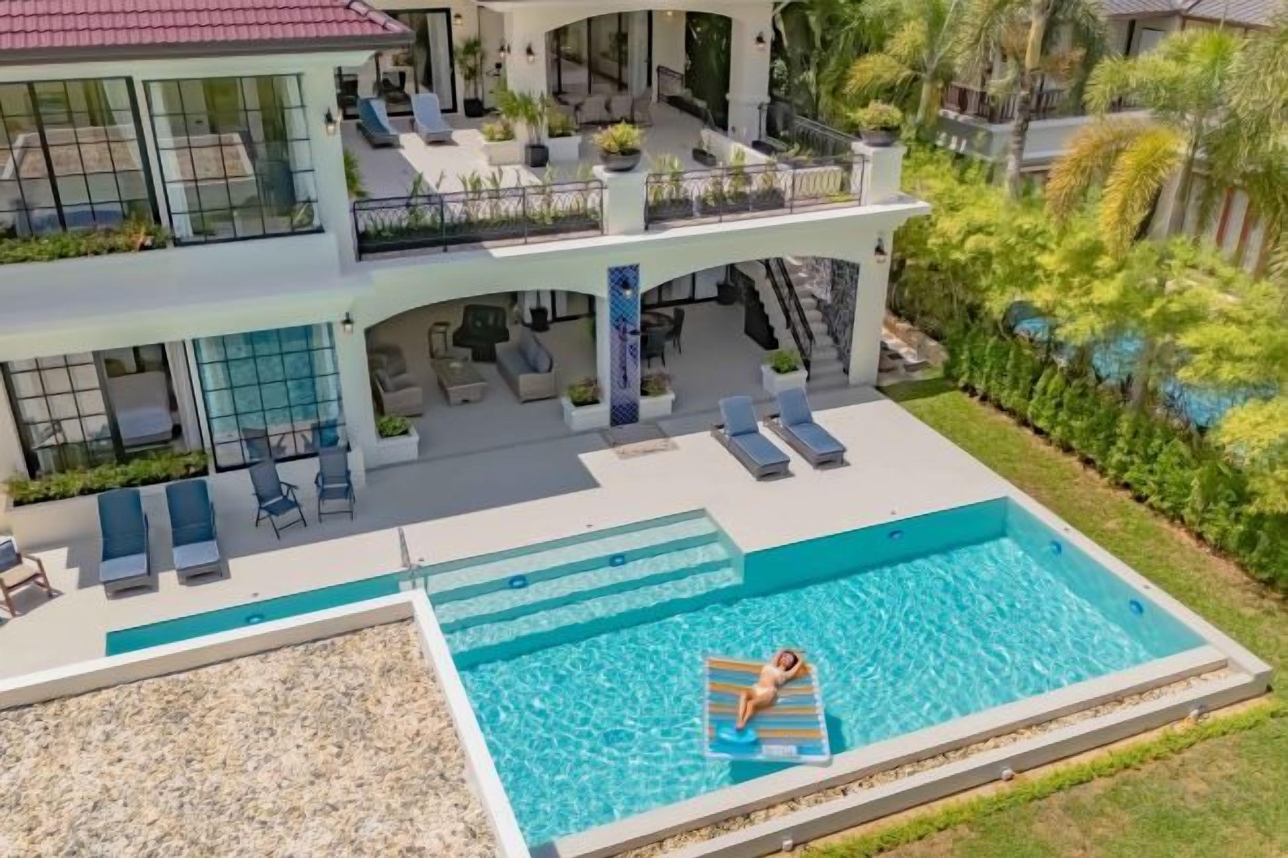 A two-story building with a swimming pool, outdoor seating, and a covered patio area.