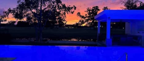 A pool area with a gazebo and a view of a sunset.