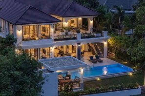 Una casa de dos pisos con piscina, mobiliario exterior y una escalera que conduce al piso superior.