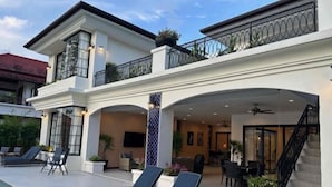 Un edificio de dos pisos con área de piscina, sillones de descanso y una escalera.