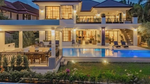 Una casa de dos pisos con piscina, mobiliario exterior e interiores bien iluminados.