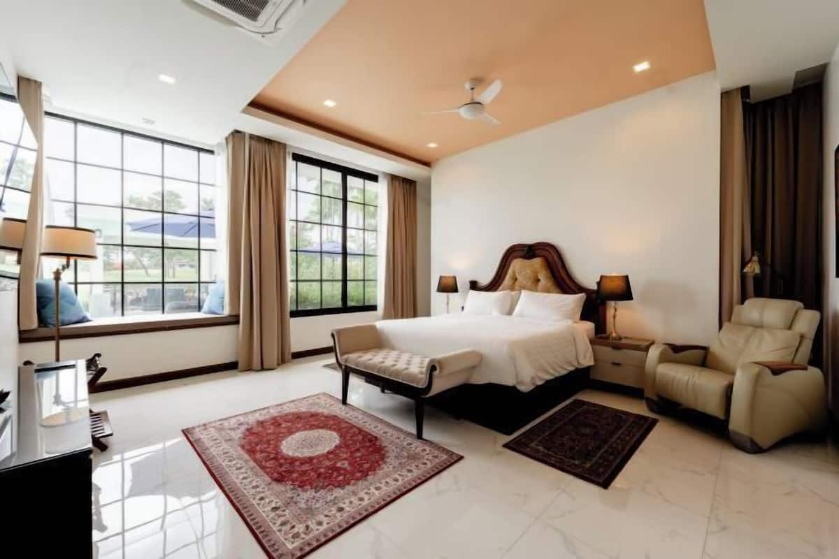 A spacious hotel room with a large bed, a sofa, a recliner, a desk, and a window with curtains.