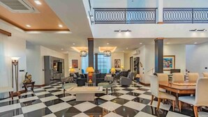 Un hall espacioso con piso de cuadros, mobiliario moderno y un balcón con barandilla.