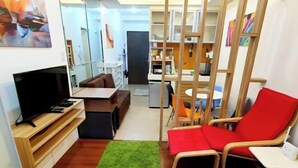 A compact living space with a television on a wooden stand, a red chair, a small table, and a green rug. - Contemporary Maison Studio Unit at Ortigas Center Pasig (Pasig)