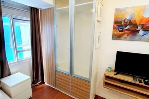 A hotel room with a sliding glass door, a flat-screen TV, and a painting on the wall. - Contemporary Maison Studio Unit at Ortigas Center Pasig (Pasig)