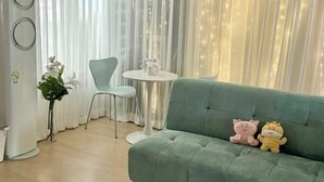 A green sofa with two plush toys, a white round table, a white chair, and a plant. - GreenNarae Stay Sadang (Seoul)
