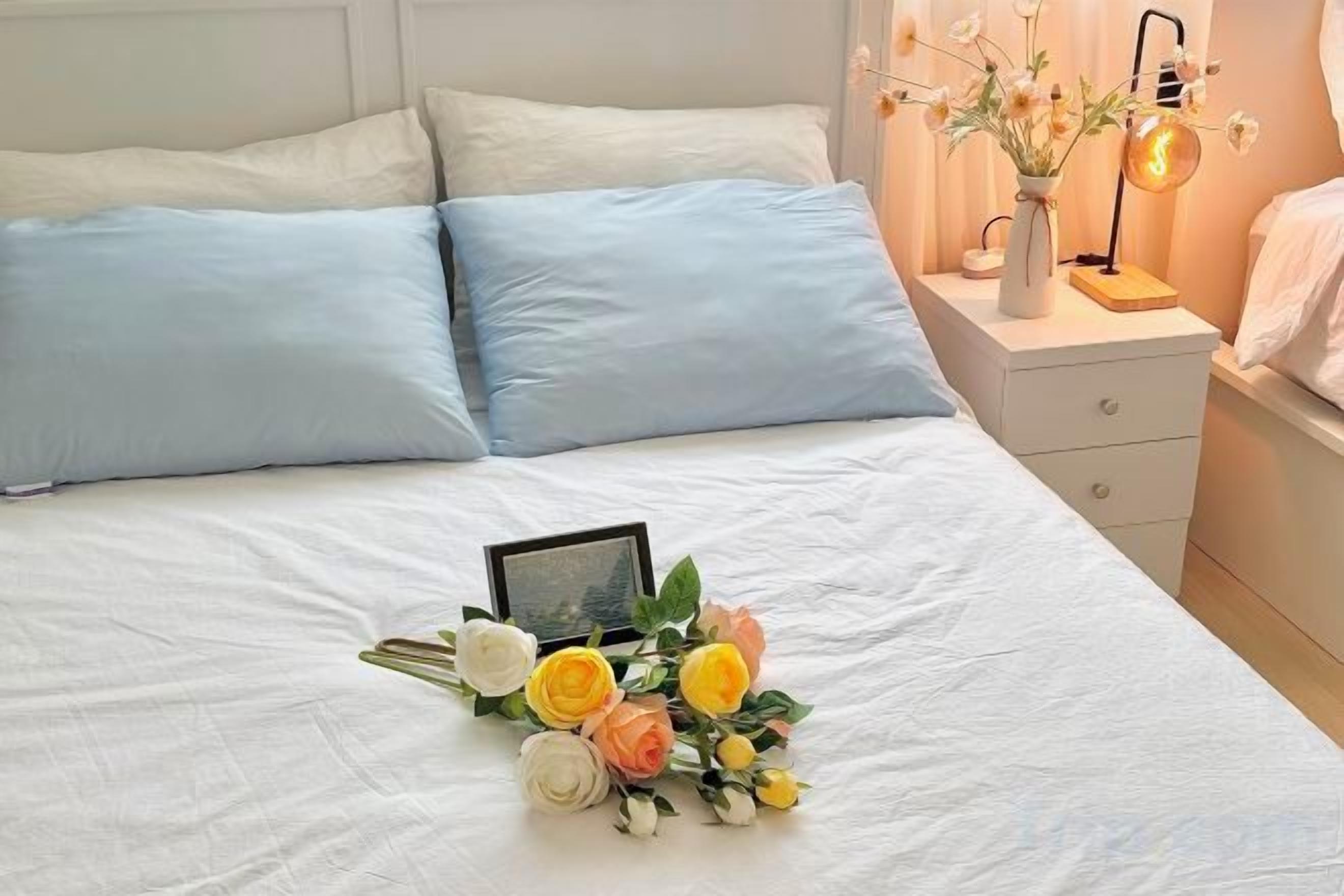 A neatly made bed with a bouquet of flowers and a framed photo on the bed.