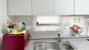 A kitchen with a stainless steel sink, white cabinets, a window with sheer curtains, and a small potted plant on the counter. - GreenNarae Stay Sadang (Seoul)