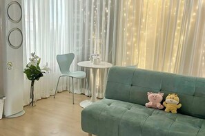 Una habitación con un sofá verde, una mesita redonda pequeña, una silla y una planta en maceta.
