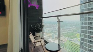 Een balkon met uitzicht op een stadsgezicht, een neonreclame en een bloempot.