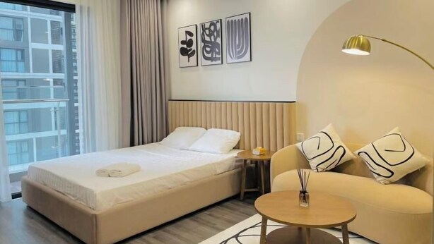 Een moderne hotelkamer met een groot bed, een slaapbank, een kleine tafel en een raam met gordijnen. Er hangen drie kunstwerken in lijsten aan de muur.