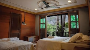 A hotel room with two beds, a ceiling fan, a window with a view of greenery, and a small table with a lamp. - Deserenity Exclusive Jungle Resort Seremban (Seremban)