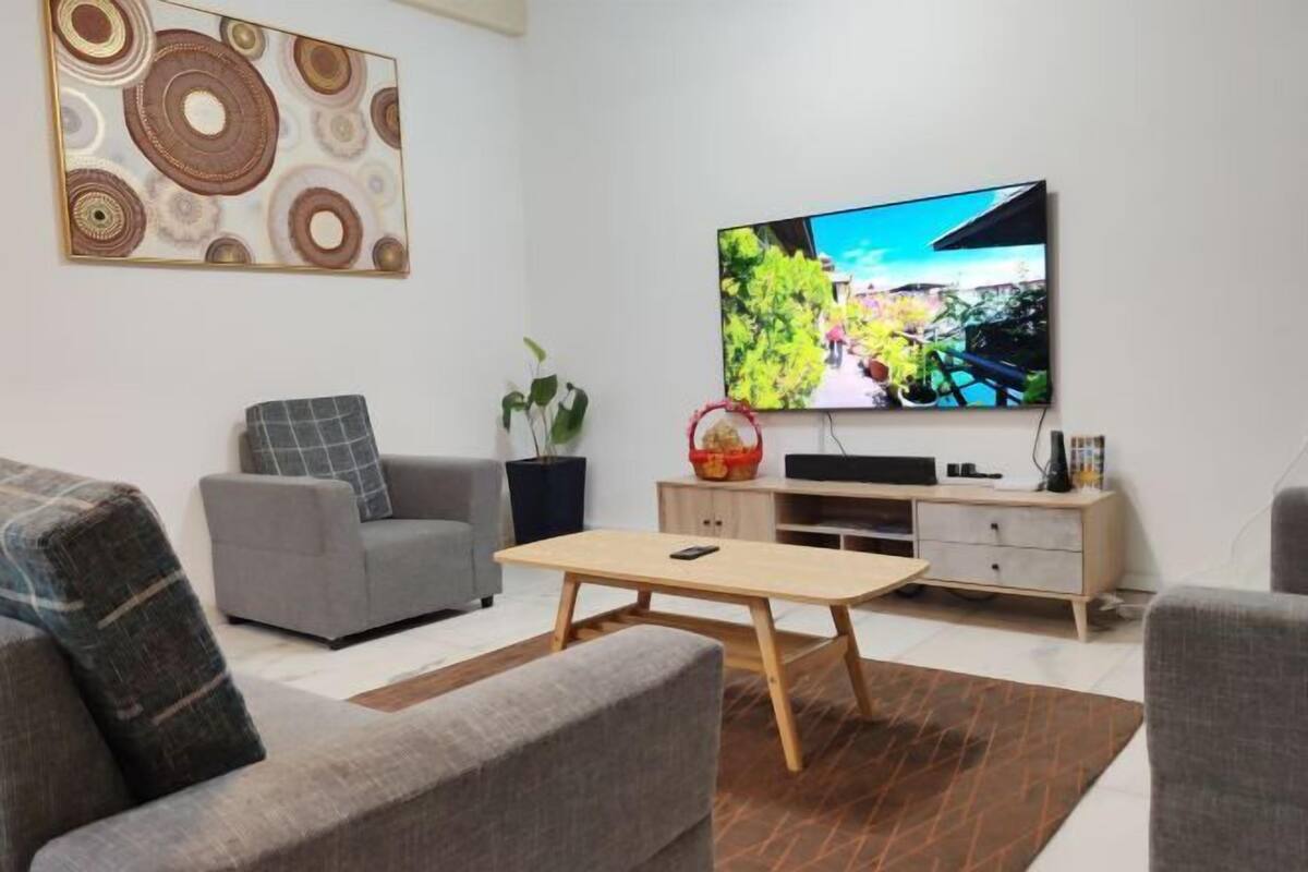 Ein modernes Wohnzimmer mit grauem Sofa, Couchtisch aus Holz, Flachbildfernseher und einer dekorativen Wandgestaltung.