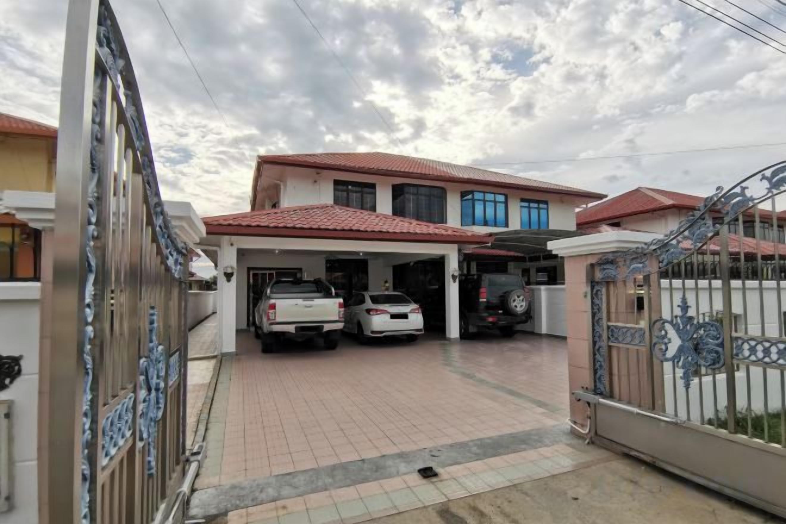 A residential property with a covered driveway, two cars parked, and a gated entrance.
