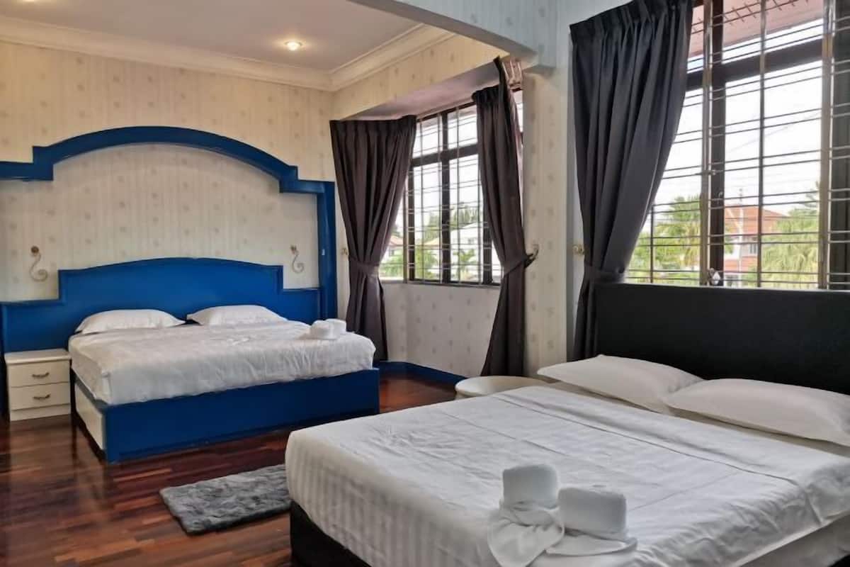 Quarto de hotel com parede azul decorativa, uma cama grande, uma cama menor, uma mesa de cabeceira, janela com cortinas e vista para vegetação lá fora.