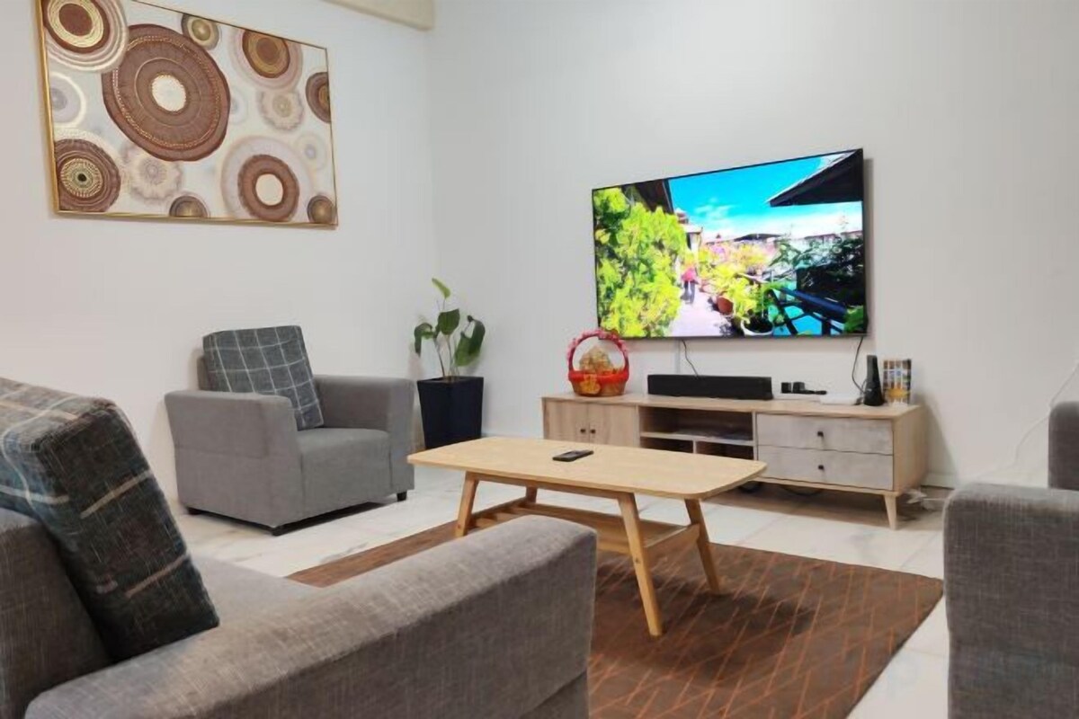 Ein Wohnzimmer mit Flachbildfernseher, grauen Sofas, einem Couchtisch und einer Wanddekoration.