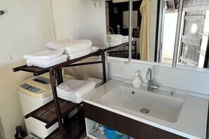 A bathroom with a white sink, a mirror, and a towel rack with folded towels. - Nukanuka ぬかぬか (Miyakojima)