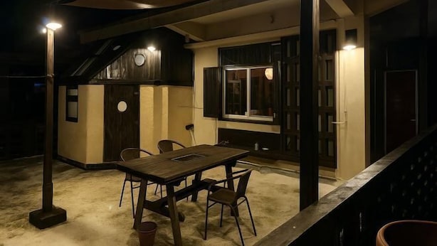 Un espace de restauration en plein air avec une table et des chaises en bois, entouré de murs percés de fenêtres et de portes.