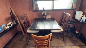 Une table à manger en bois avec des chaises, une fenêtre avec des rideaux et une petite étagère avec quelques objets.