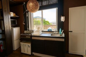 A kitchen with a microwave, refrigerator, sink, and a hanging light fixture. - Nukanuka ぬかぬか (Miyakojima)