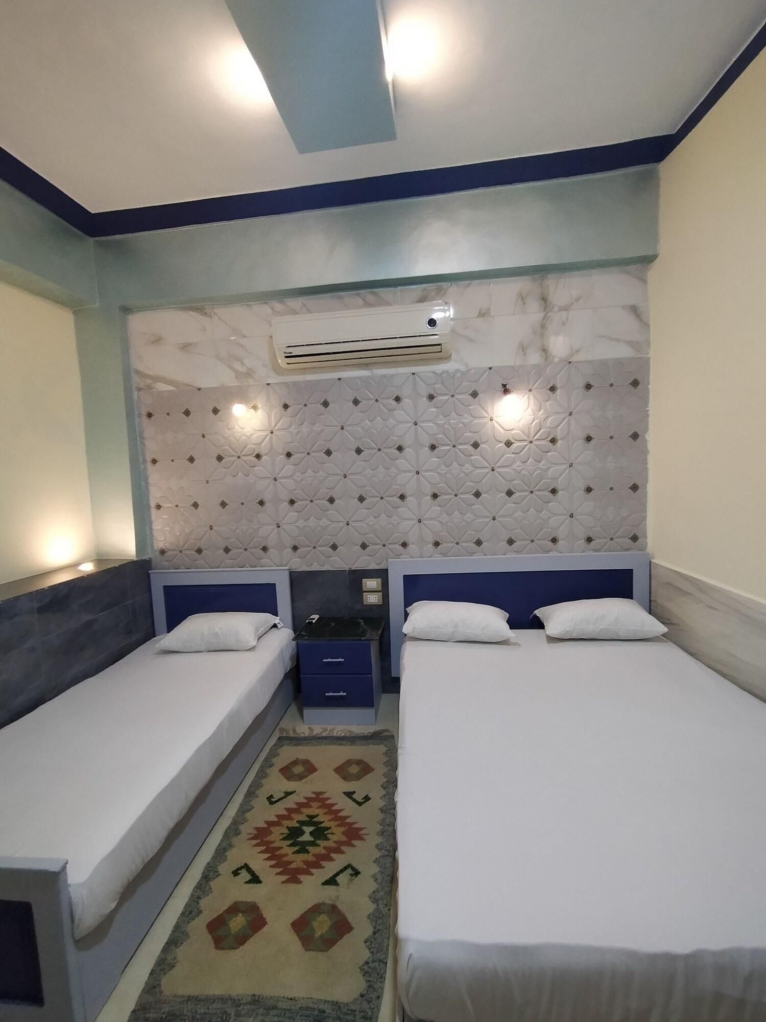 A hotel room with two single beds, a patterned rug, a wall-mounted air conditioner, and a decorative headboard.