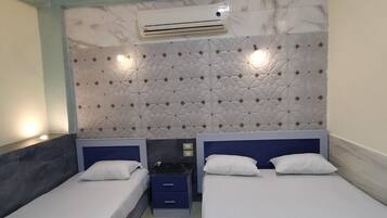 A hotel room with two single beds, a patterned rug, a wall-mounted air conditioner, and a decorative headboard.
