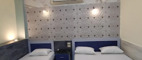 A hotel room with two single beds, a patterned rug, a wall-mounted air conditioner, and a decorative headboard.