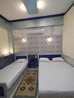 Habitación de hotel con dos camas individuales, una alfombra estampada, un aire acondicionado de pared y un cabecero decorativo.