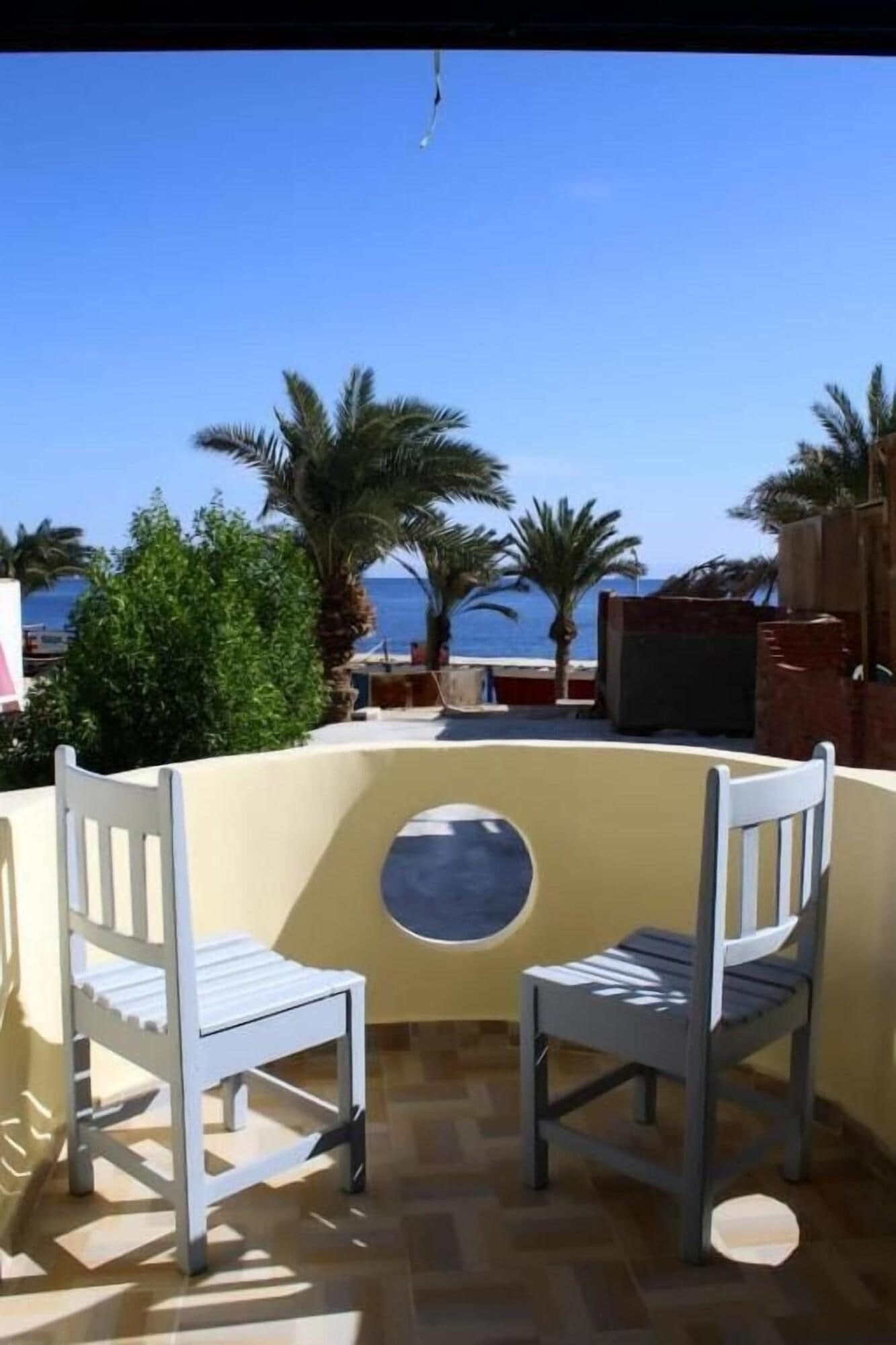 Un patio con dos sillas blancas, una mesa redonda y vista al mar.
