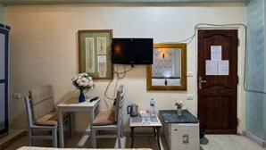Una camera d'albergo con un letto, una scrivania con una sedia, una televisione, un tavolino con un vaso di fiori e una porta con un avviso.